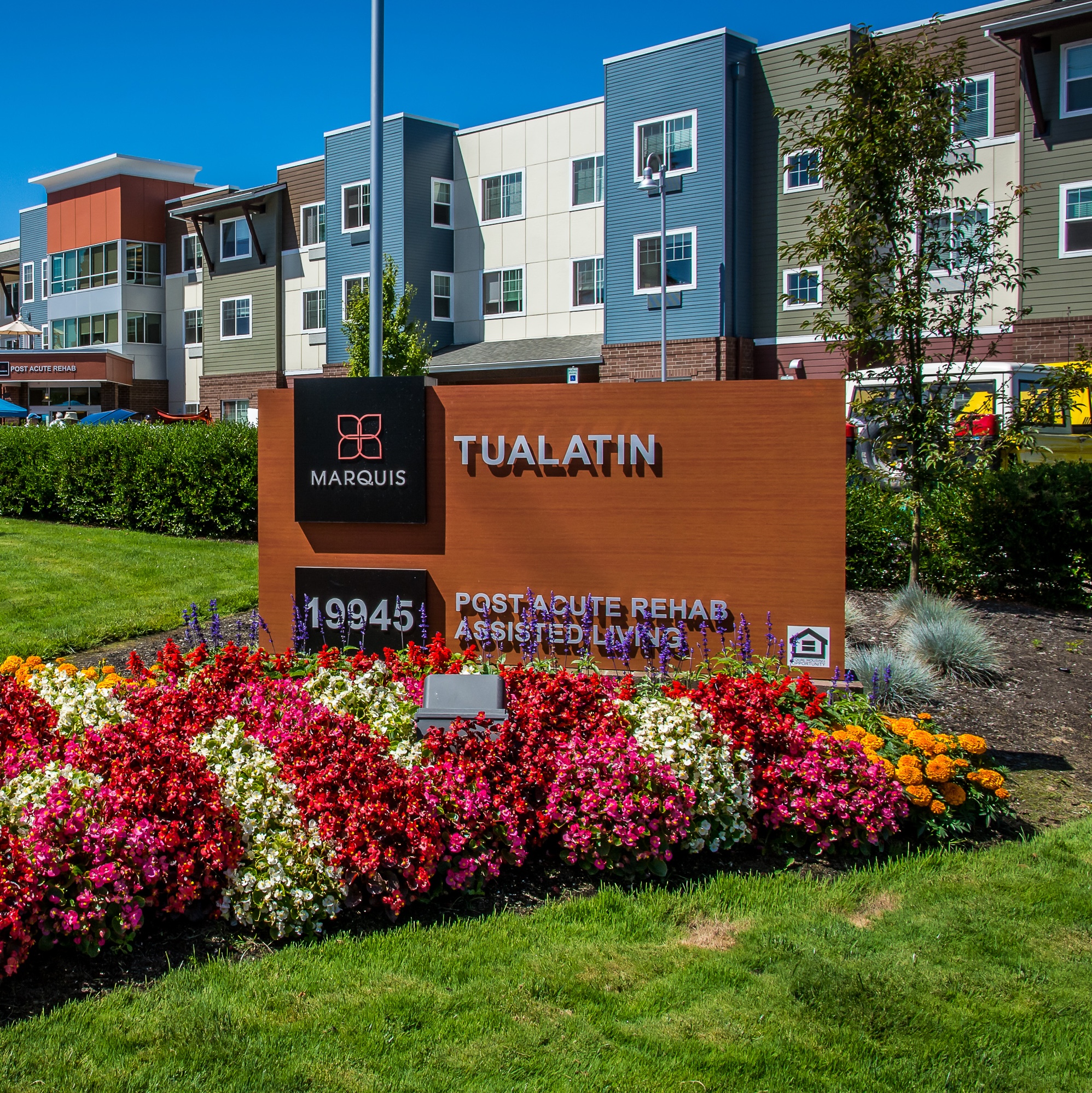 Marquis Tualatin Post Acute Rehab and Assisted Living community entrance sign surrounded by colorful flowers in front of the modern senior care facility